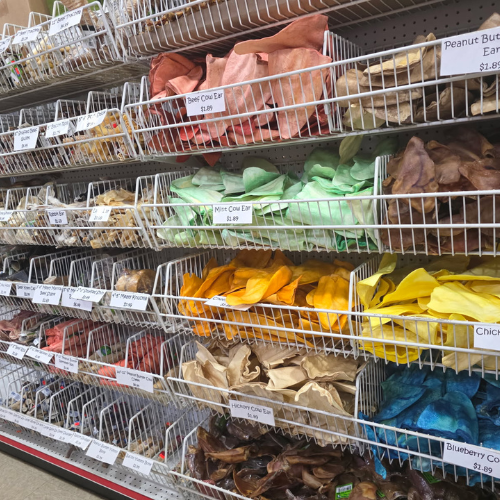 Shelves of colorful pet treats in a store, organized by hue. Each type is labeled, creating a vibrant and organized display.