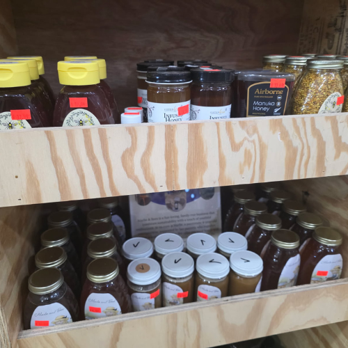 Wooden shelves display assorted honey jars with colorful labels and bright lids. Various sizes, including small jars with black labels, convey a cozy, rustic feel.