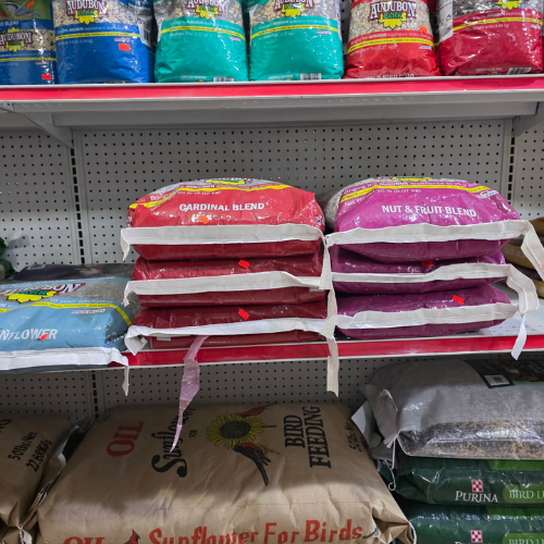 Shelves stocked with various bird seed bags, including cardinal blend, nut & fruit blend, and sunflower seed. The scene conveys variety and abundance.