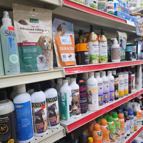 Image of a pet store aisle displaying various pet grooming products on shelves. Bottles and packaging feature images of cats and dogs, conveying a clean and organized setting.