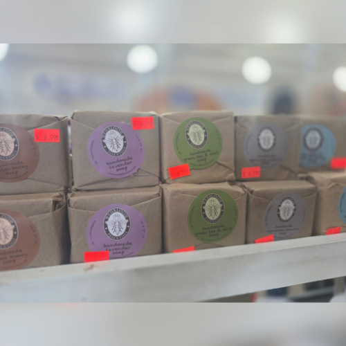 Wrapped soap bars on display, each with colorful round labels and red price tags. The setting is a well-lit store shelf, conveying a neat, inviting ambiance.